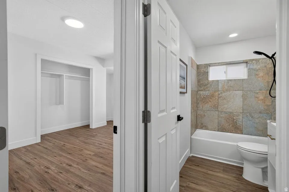 Bathroom featuring a tub and shower combination with stone tile surround, window, and toilet
