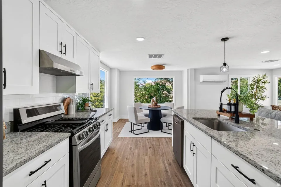 White shaker cabinetry, stainless steel appliances, speckled stone countertops, wood-finish flooring, and a subway tile backsplash