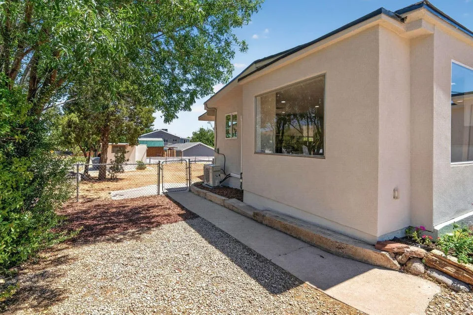 Stucco exterior, expansive windows, concrete walkway, chain-link fencing, mature tree