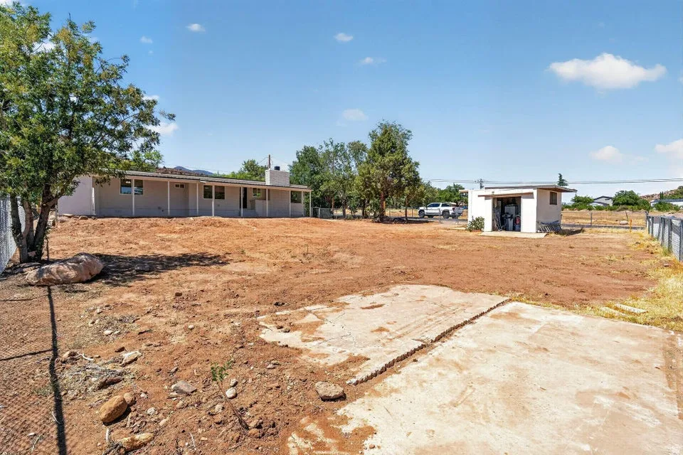Expansive property featuring a single-story residence with a covered patio, a detached utility building, and a chain-link fence