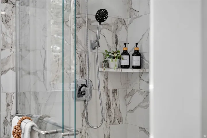 Shower with marble-look tile surround, glass enclosure, and a built-in recessed shelf