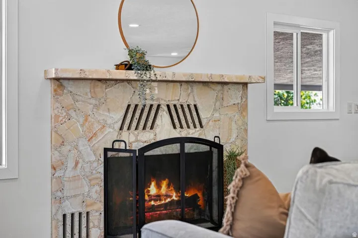 Stone surround fireplace with a metal screen and mantel, accompanied by a white-framed window