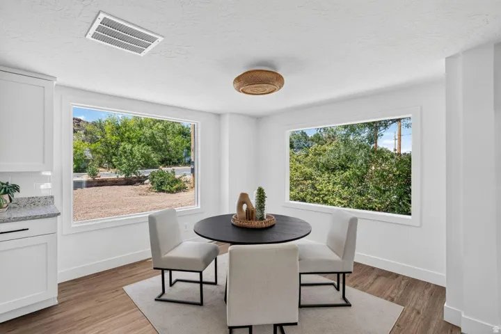 White cabinetry with granite countertop, wood-finish flooring, two large windows, and a ceiling-mounted light fixture