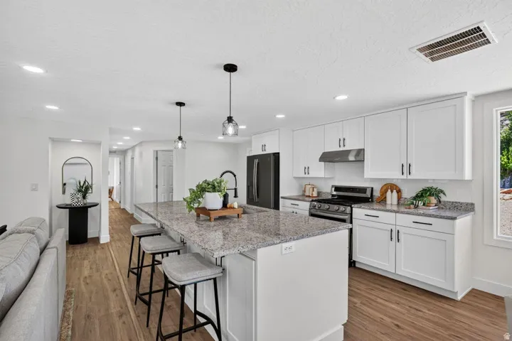 Open-concept kitchen featuring white shaker cabinetry, granite countertops, a center island with seating, and wood-finish flooring