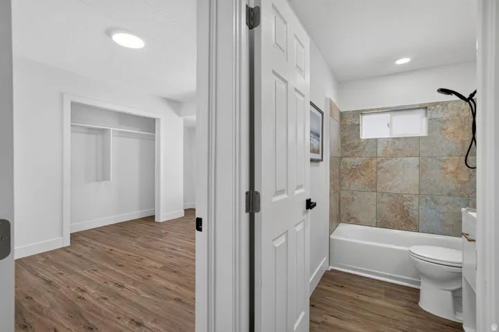 Bathroom featuring a tub and shower combination with stone tile surround, window, and toilet