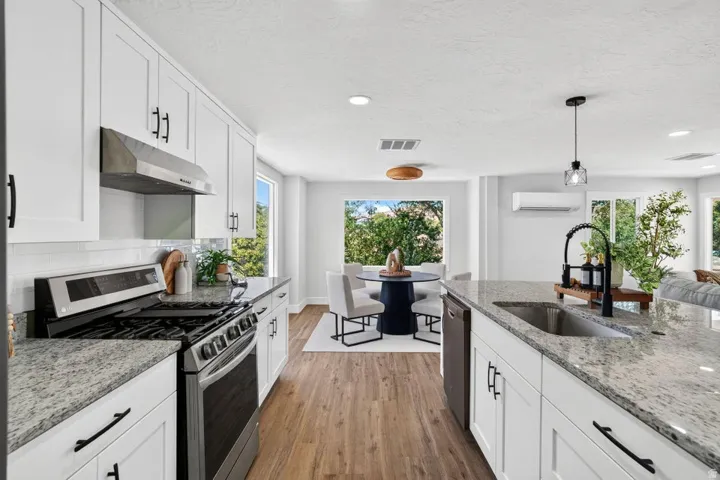 White shaker cabinetry, stainless steel appliances, speckled stone countertops, wood-finish flooring, and a subway tile backsplash