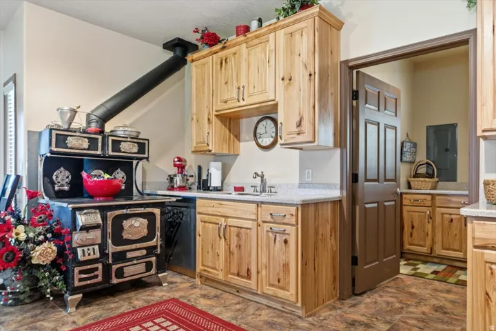 Wood-finish flooring, custom wood cabinetry, light-toned countertops, stainless steel sink, and a prominent wood-burning stove