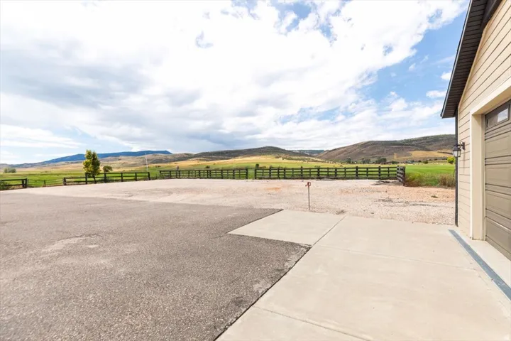 Expansive gravel and asphalt parking area with concrete walkways, surrounded by a dark-stained wooden fence, and backed by a scenic hilly landscape