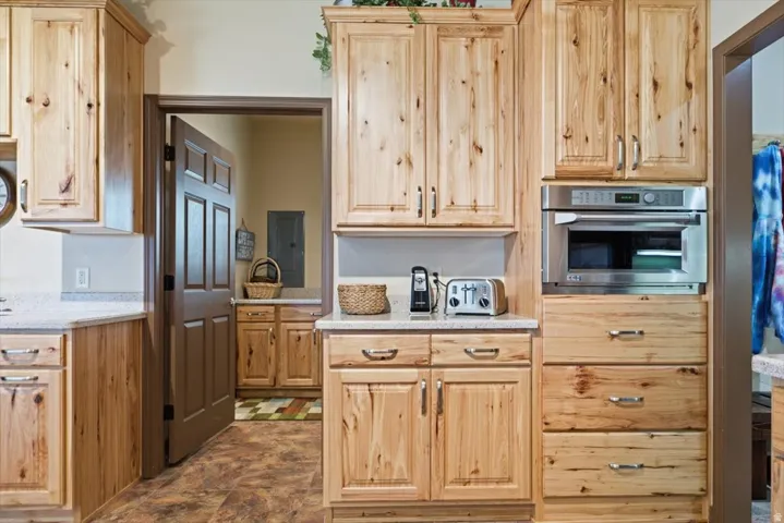 Wood cabinetry, light-toned countertops, built-in stainless steel microwave, and wood-finish flooring