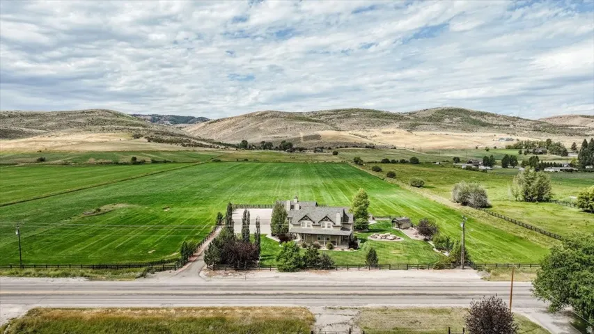 Expansive property featuring a multi-story residence with a gabled roof, surrounded by extensive green fields and mature landscaping