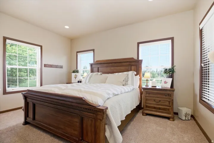 Recessed ceiling lighting illuminates a carpeted room featuring multiple windows with blinds and wood-trim casings