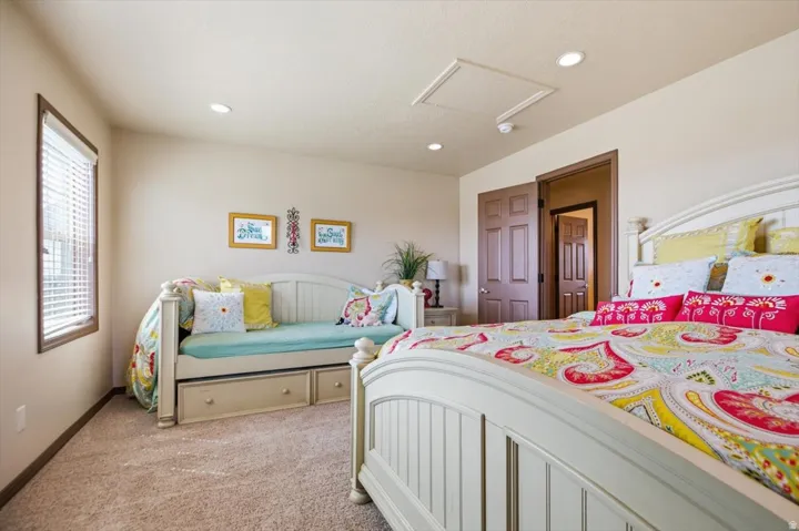 Recessed lighting illuminates this room, featuring light-colored carpeting, a window with horizontal blinds, and a paneled door