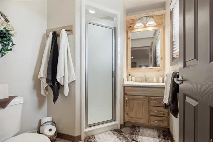 Walk-in shower with frosted glass enclosure, wood-finish vanity with countertop sink, and wall-mounted light fixture