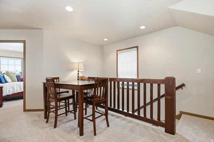 Carpeted landing featuring a wood-finish railing and window with blinds
