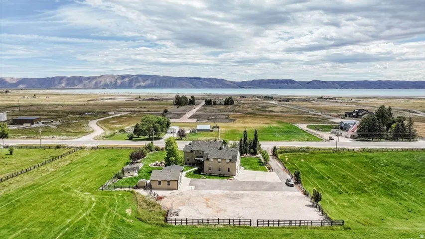 Property with expansive green fields, a substantial main residence, an auxiliary structure, and a large unpaved parking area