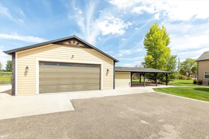 Detached garage featuring a paneled door with upper windows, concrete driveway, and covered carport
