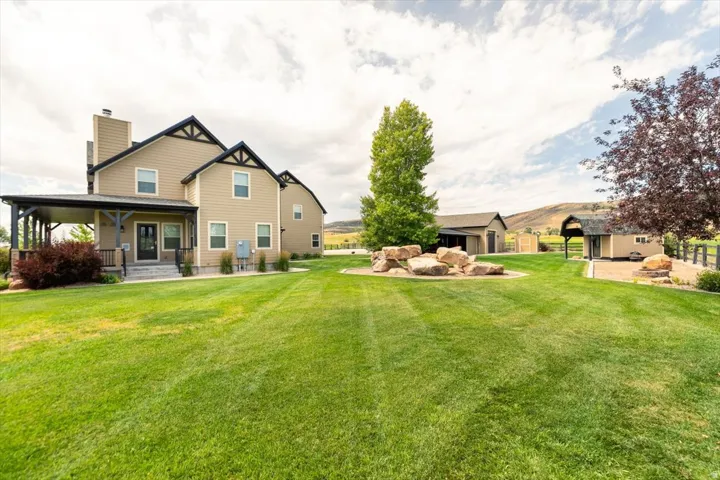 Spacious green yard with decorative boulders, expansive covered porch, and detached outbuilding