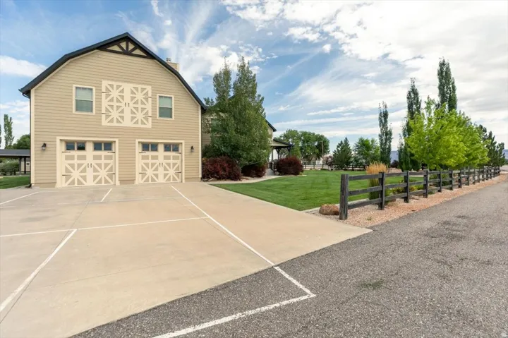 Barn-style residence featuring dual garage doors with decorative overlays, a concrete driveway, a manicured lawn, and a dark wood-finish fence