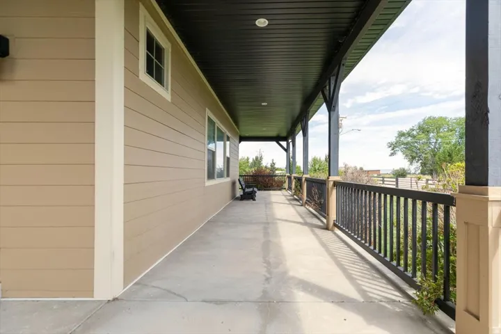 Expansive covered porch featuring a concrete surface, dark ceiling, and a dark railing with decorative metal inserts
