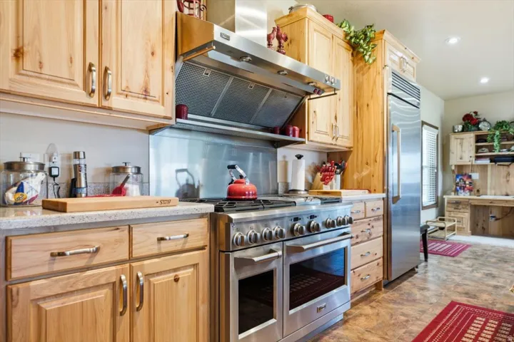 Stainless steel appliances, wood cabinetry, stone-finish countertops, stainless steel backsplash, and wood-finish flooring