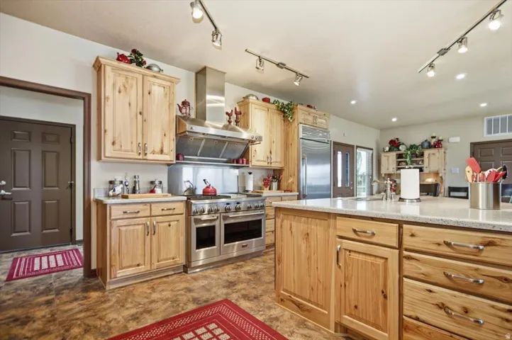Spacious kitchen featuring light wood cabinetry, stone-finish countertops, stainless steel appliances, and track lighting