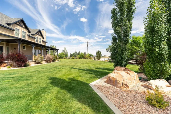 Expansive green lawn with a large residence featuring a covered front porch, decorative pillars, and dormer windows