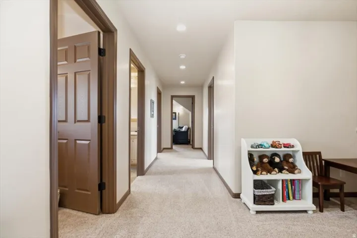 Hallway with recessed lighting, light-colored carpeting, multiple doorways, and neutral wall tones