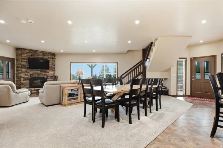 Stone-faced fireplace, large picture window, recessed lighting, wood staircase with railing, and a multi-panel entry door