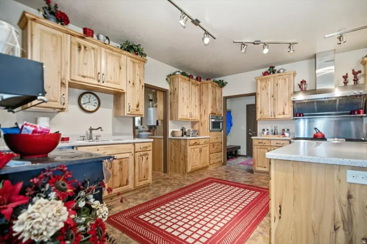 Kitchen featuring natural wood cabinetry, light-toned countertops, stainless steel range hood, stainless steel wall oven, and track lighting