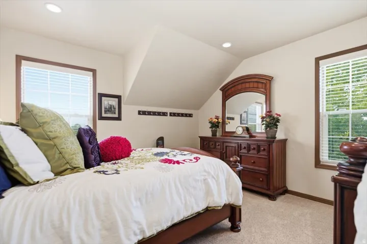Recessed lighting, sloped ceiling, wood-trimmed windows, wall-mounted coat rack, and a neutral carpeted floor