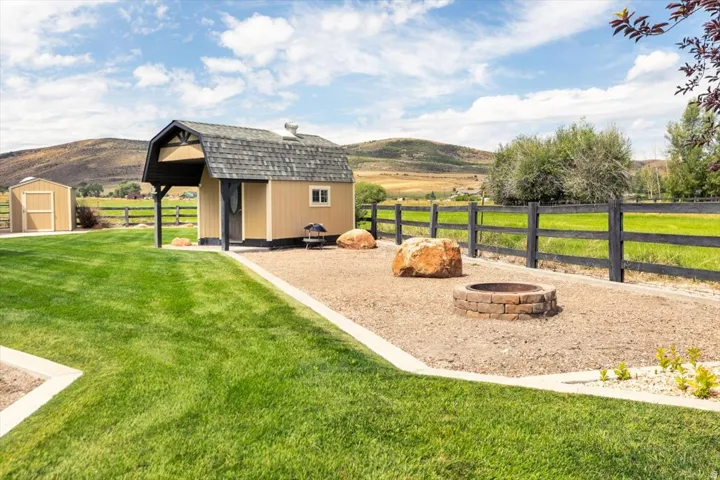 Manicured lawn with a detached shed, a secondary storage shed, a defined gravel area with a fire pit, and a dark-toned fence