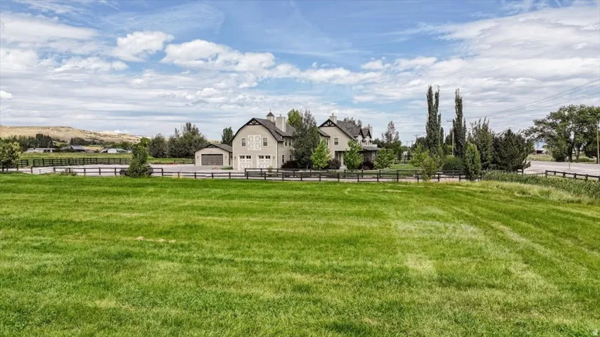 Expansive grassy area with a distant two-story residence featuring multiple dormers and a detached garage
