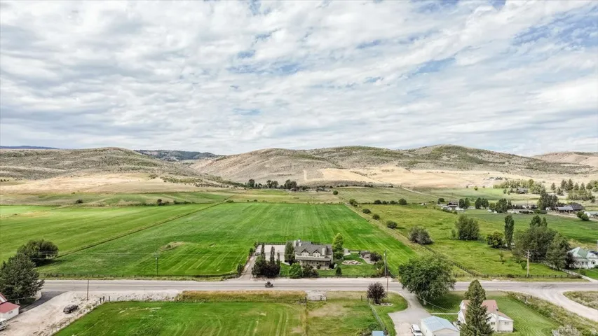 Expansive green fields, a substantial main residence, mature landscaping, and surrounding hillsides