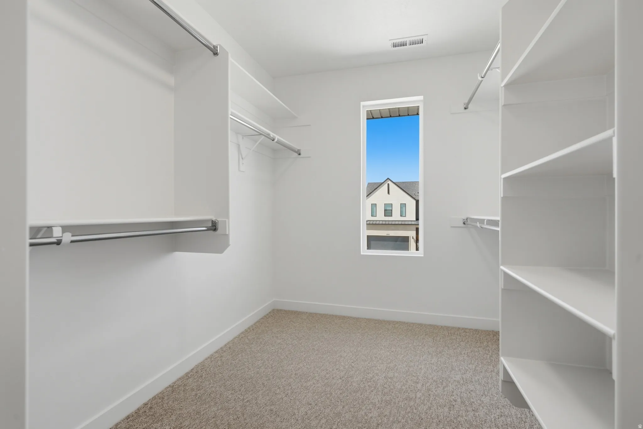 Carpeted closet space featuring built-in shelving, hanging rods, and a window for natural light