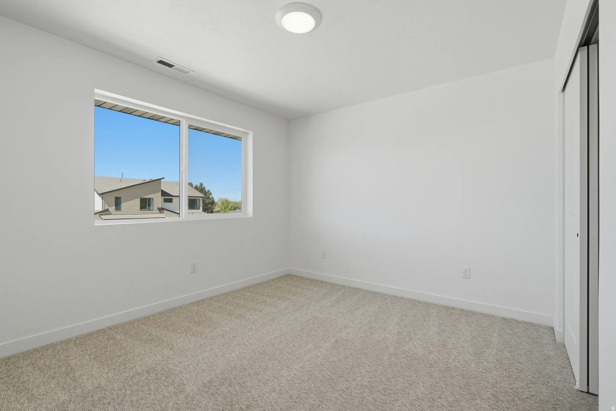 Carpeted room featuring a large window, white walls, and a flush-mount ceiling light