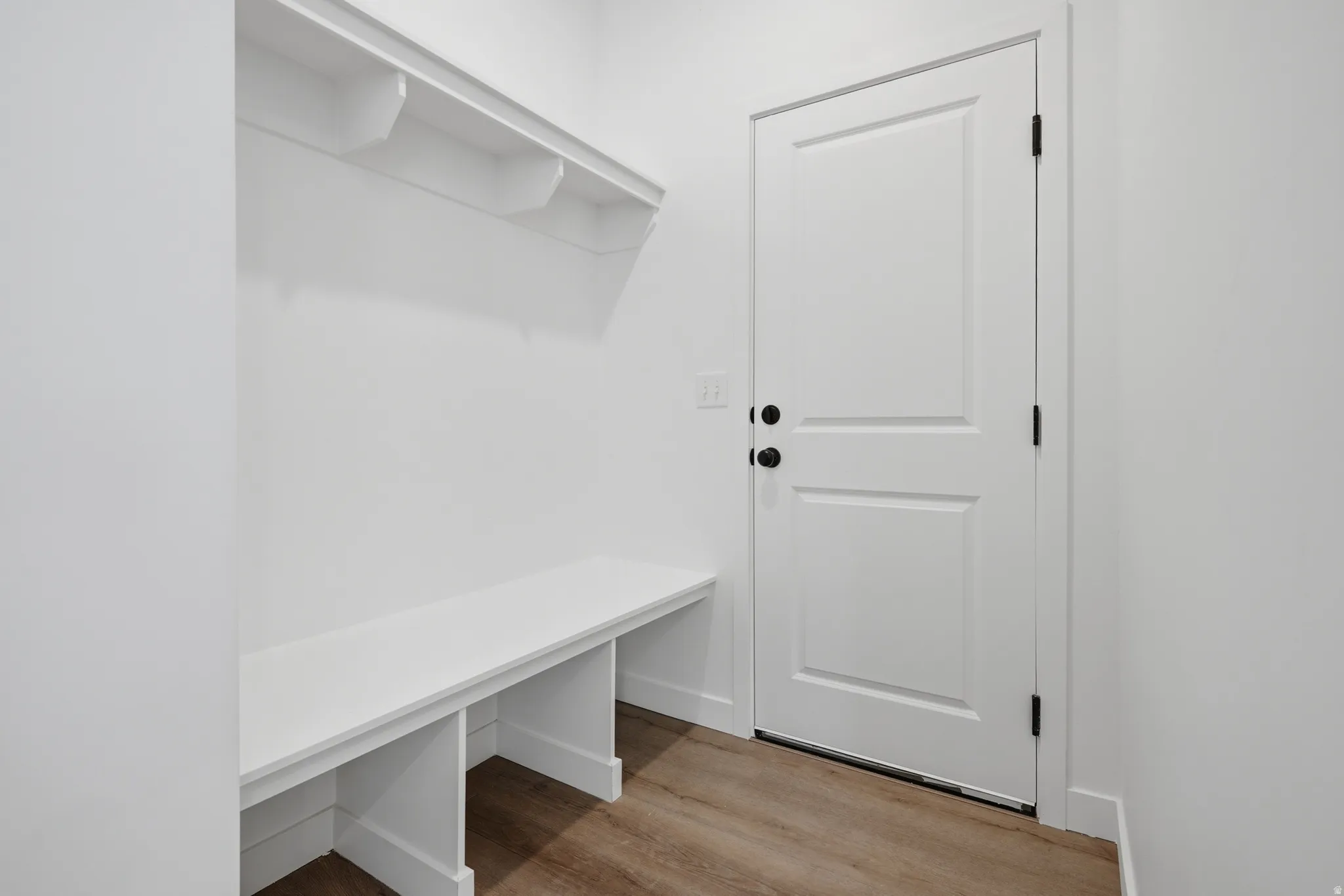 Built-in bench with upper shelving, wood-finish flooring, and a white panel door with matte black hardware
