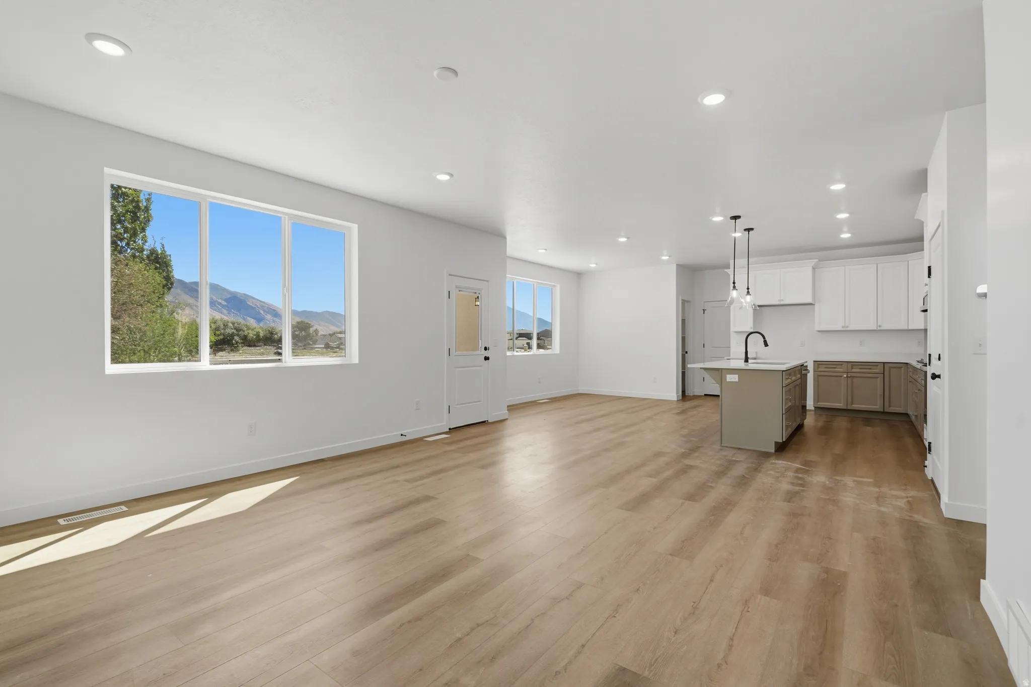 Open-concept living area featuring wood-finish flooring, recessed lighting, and a kitchen with an island, pendant lighting, and white and gray cabinetry