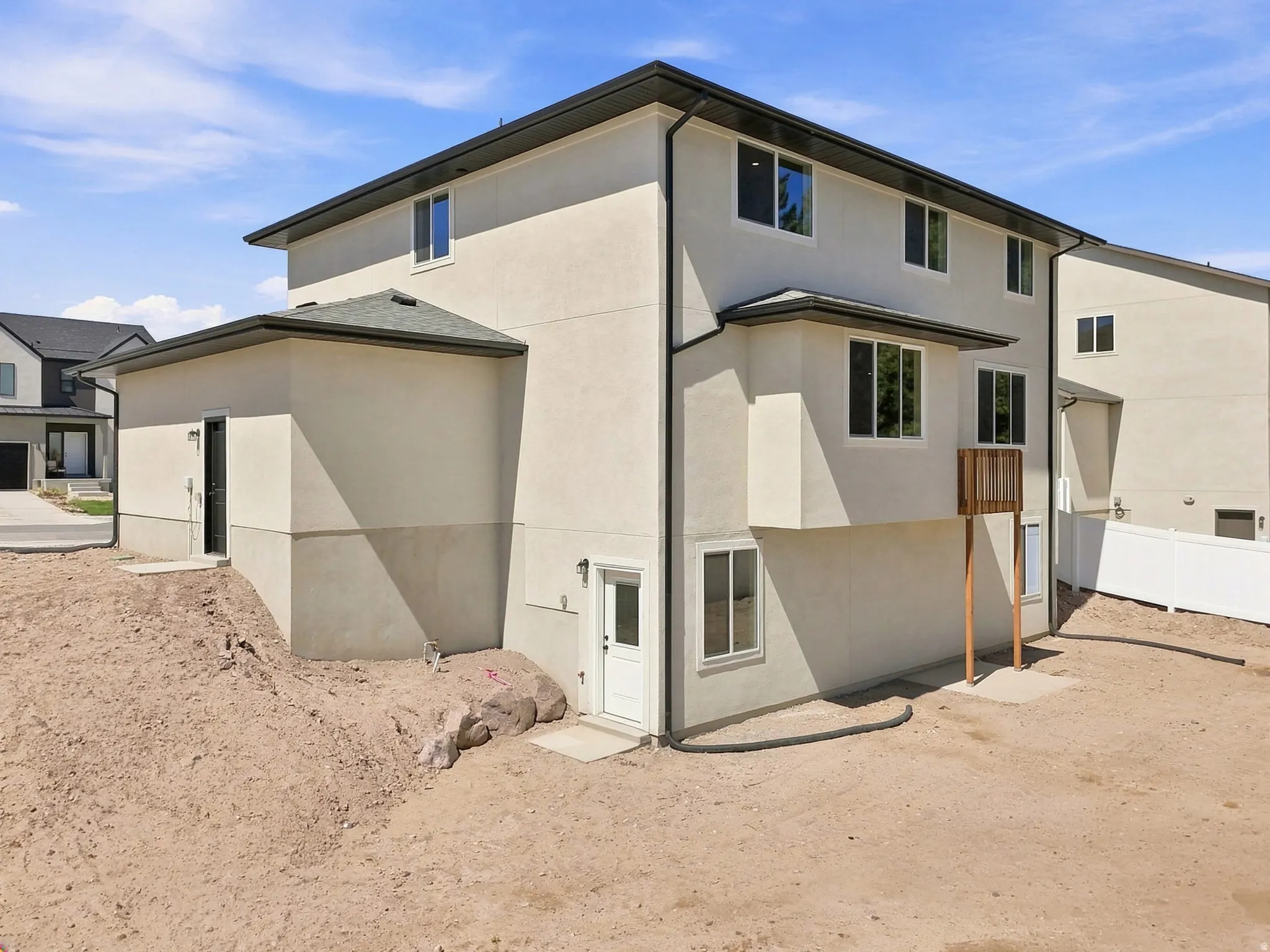Two-story stucco exterior with multiple windows, featuring a lower-level entry door and a second-story deck structure