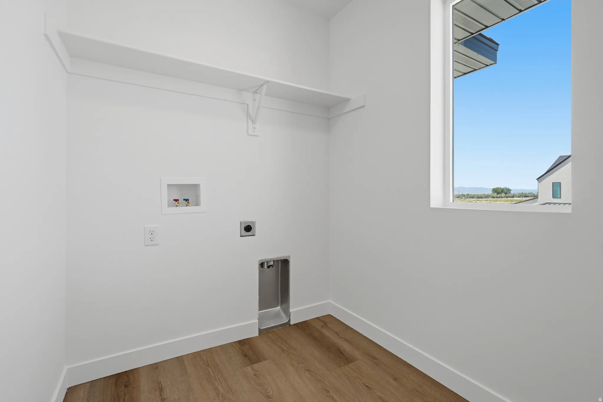 Dedicated laundry space featuring a window, built-in shelving, wood-finish flooring, and white trim