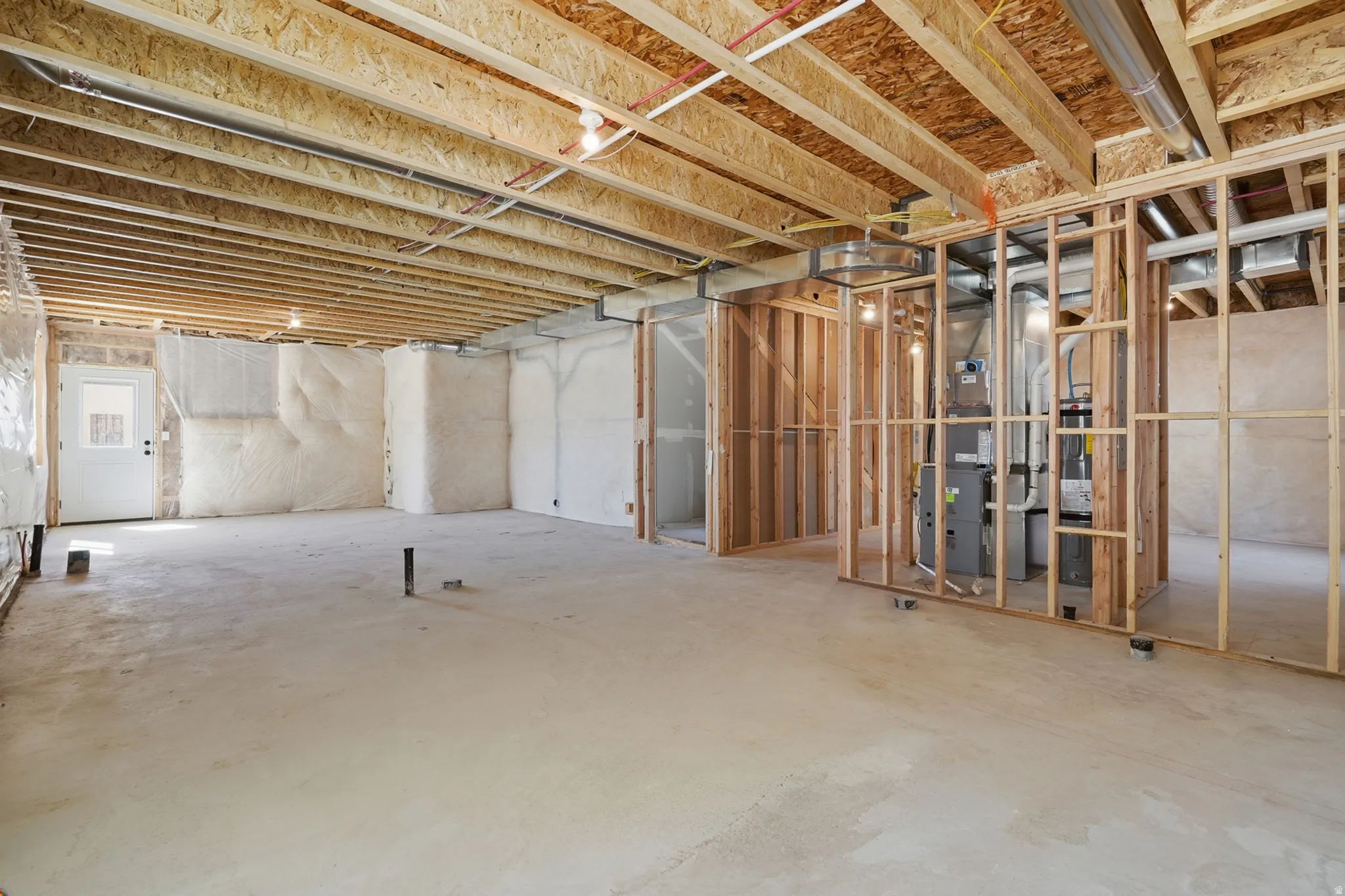 Unfinished basement featuring exposed wood framing, concrete flooring, and an exterior door with a window