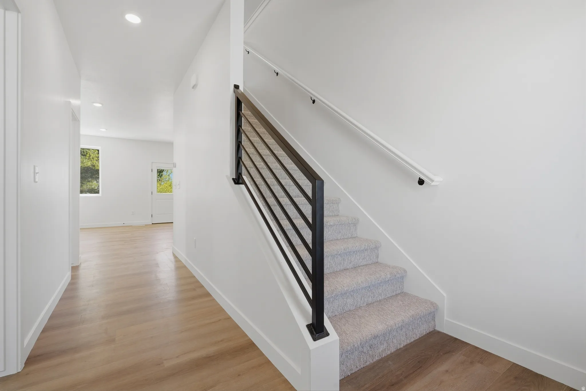 Contemporary staircase with black metal horizontal balusters, white handrail, and light-toned carpeted treads