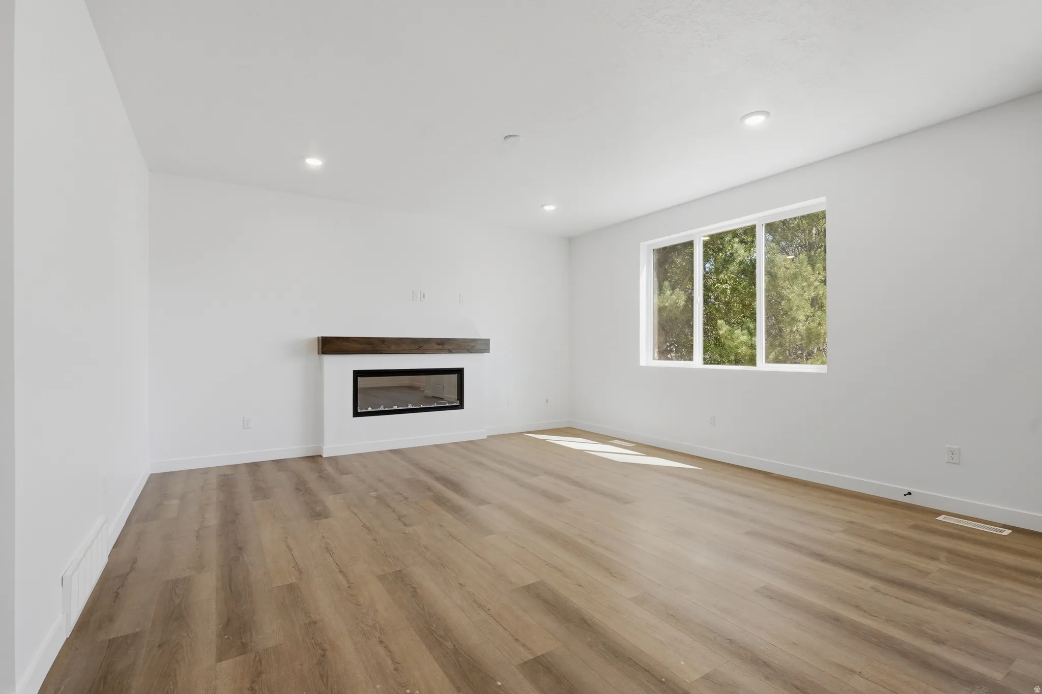 Recessed lighting, wood-finish flooring, and a modern fireplace with a wood mantel