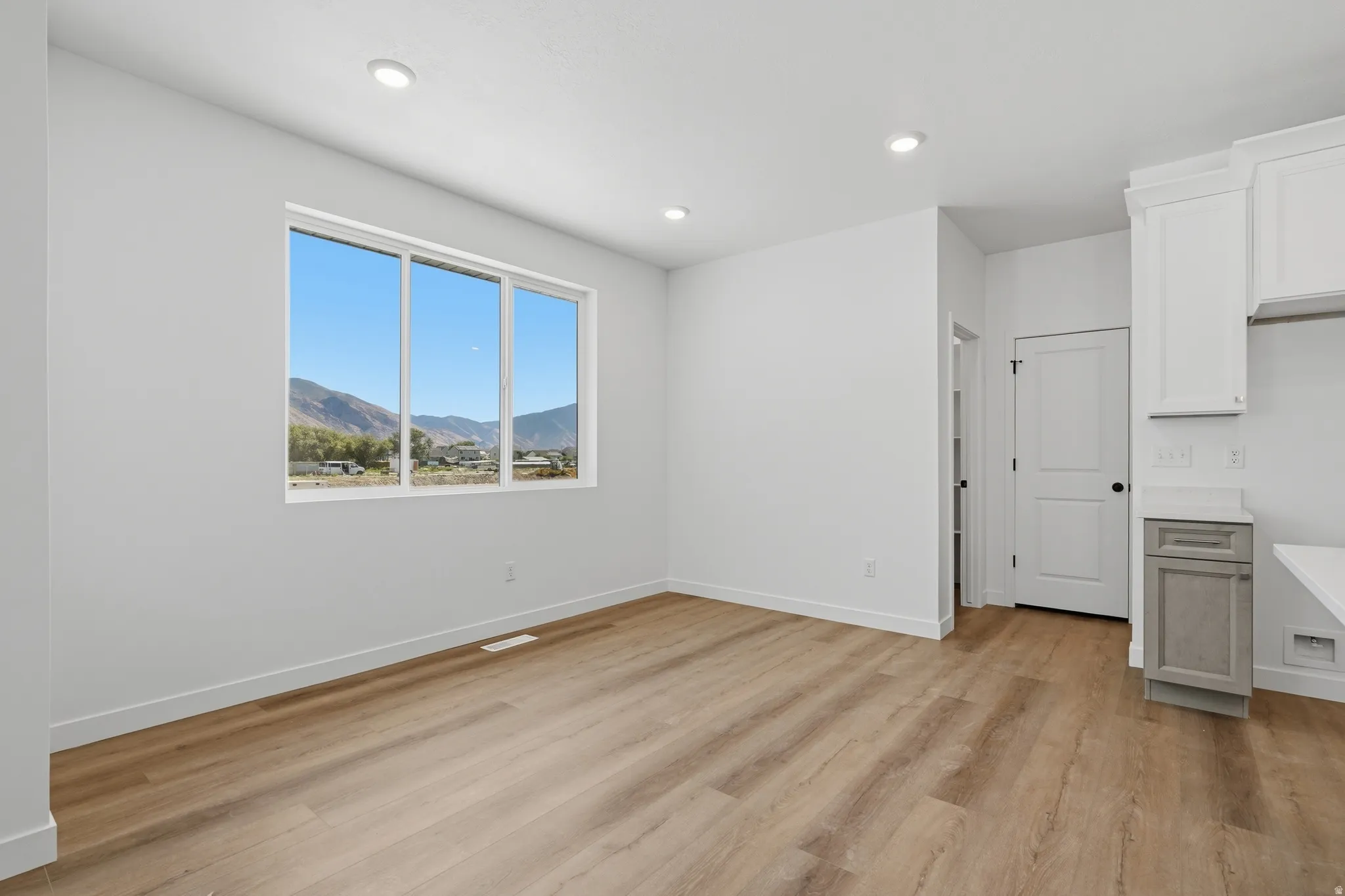 Expansive window framing a mountain backdrop, recessed ceiling lighting, wood-finish flooring, white cabinetry, and a light-toned countertop