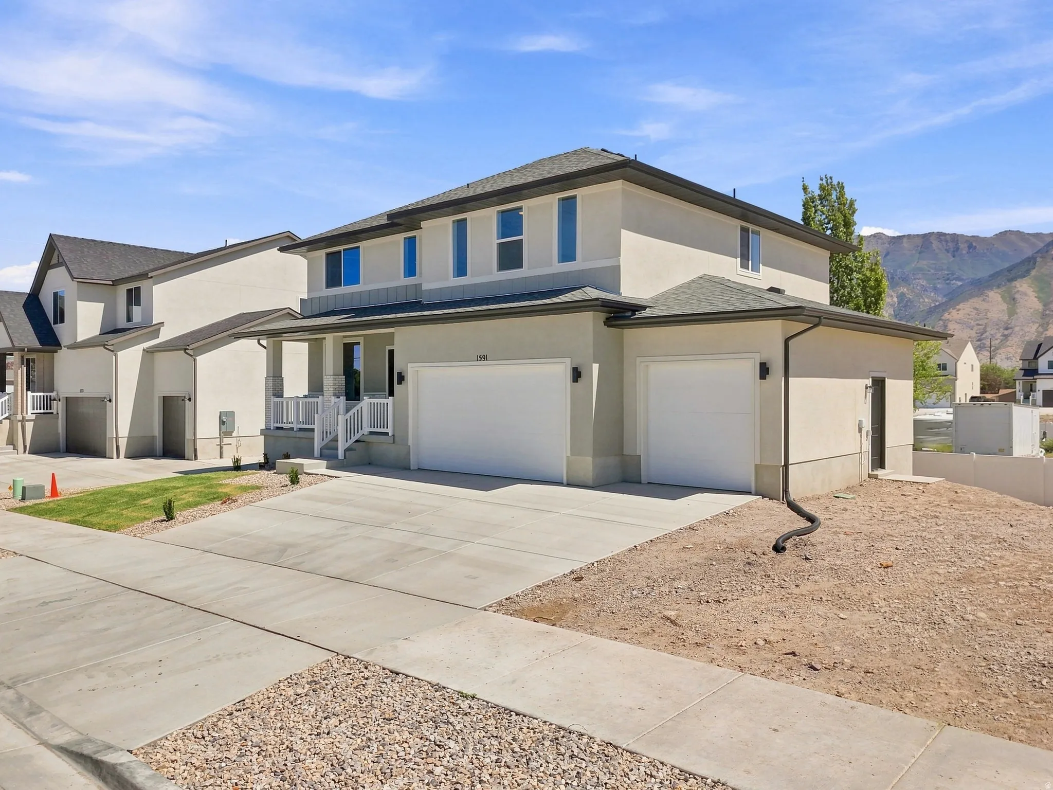 Two-story stucco exterior, two attached garages, covered front porch with white railings, concrete driveway, and a visible sidewalk