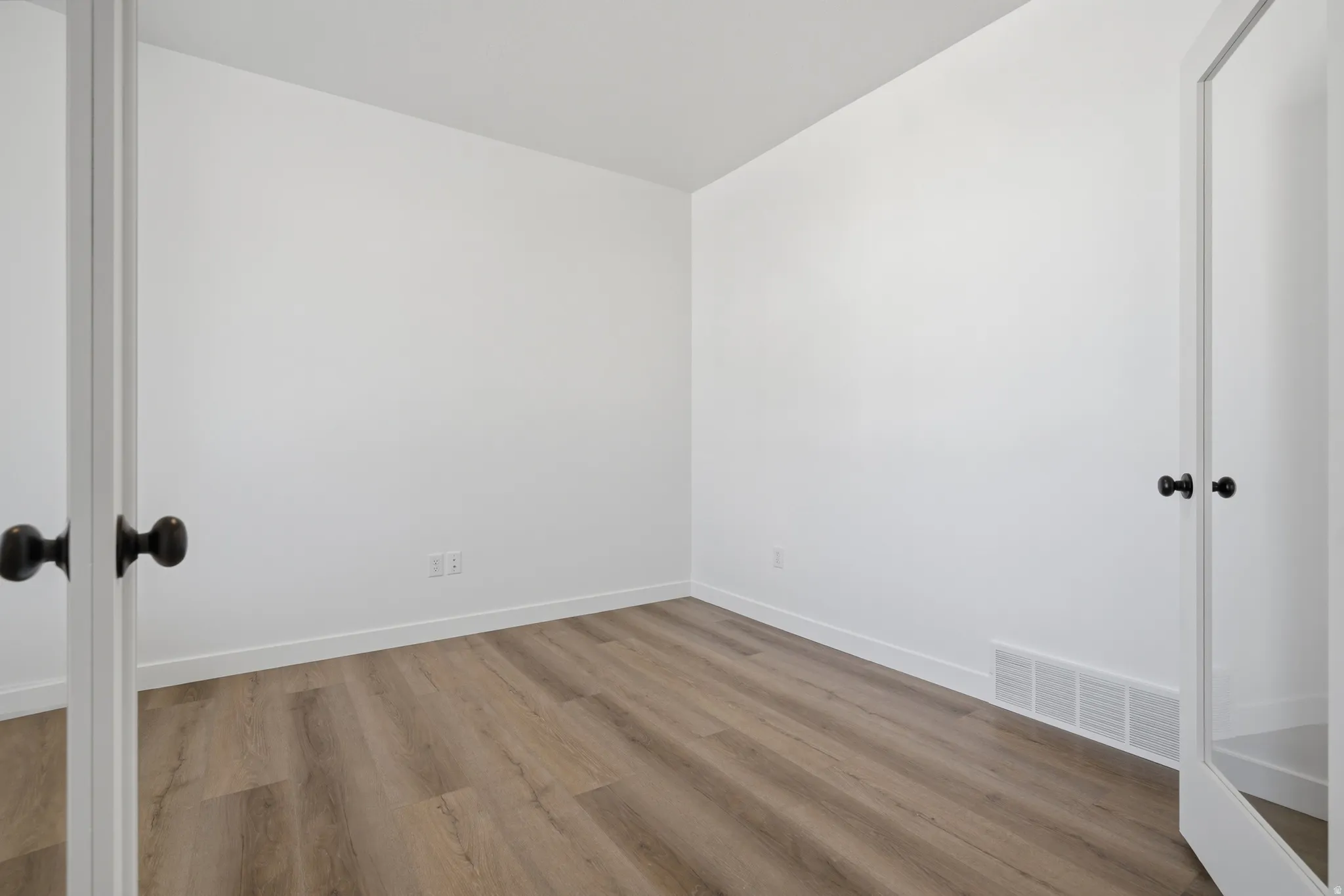 Wood-finish flooring, white walls, and a white door with a black knob