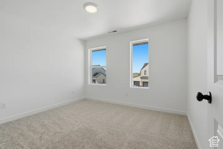 Recessed ceiling light fixture, two vertical windows, light neutral carpeting, white interior walls, and a white door with a black doorknob