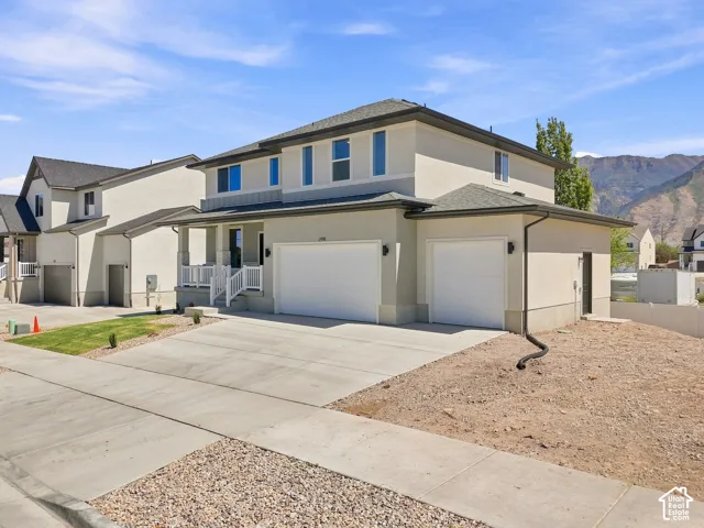 Two-story stucco exterior, two attached garages, covered front porch with white railings, concrete driveway, and a visible sidewalk