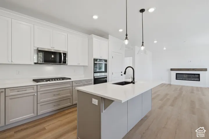 Kitchen with two-tone cabinetry, stainless steel appliances, a large island with a sink, pendant lighting, and wood-finish flooring extending into the living area with a fireplace
