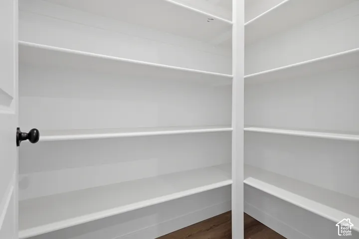 Walk-in pantry with extensive white shelving, wood-finish flooring, and a white paneled door with a black knob