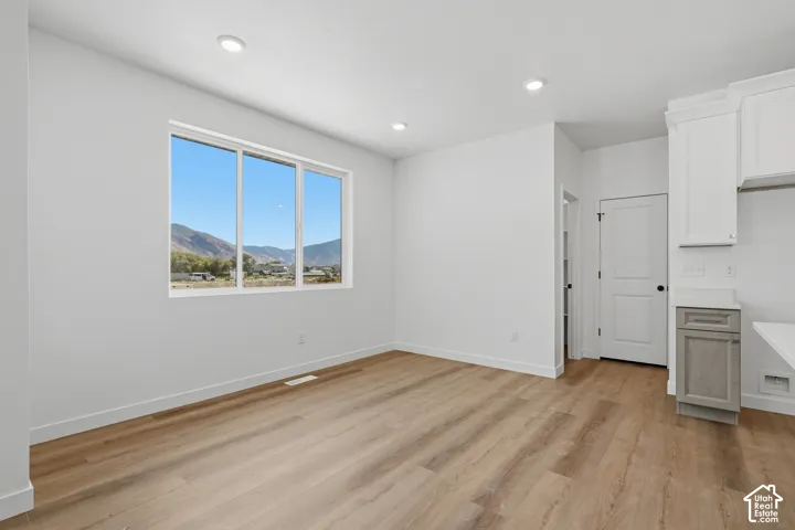 Expansive window framing a mountain backdrop, recessed ceiling lighting, wood-finish flooring, white cabinetry, and a light-toned countertop